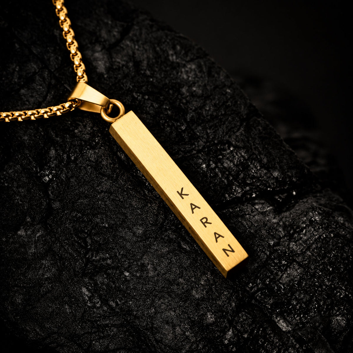 Gold name bar pendant on dark stone, engraved name close-up