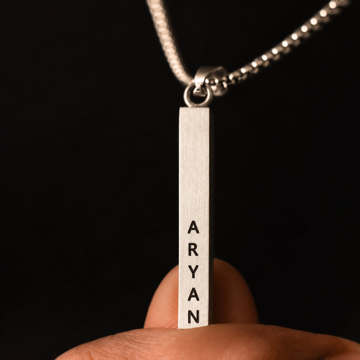 Silver name bar pendant held between fingers, engraving detail
